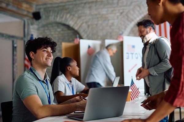 young man and woman smiling and assisting people voting at a polling site